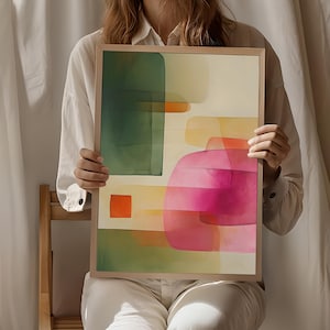 Op de afbeelding: Abstracte kunstafdruk met een aquarelontwerp. Het heeft groene, roze, oranje en gele vormen, omlijst in een lichtgekleurde houten lijst. Het thema is modern en minimalistisch.