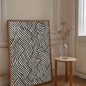 Black and white abstract line art poster featuring bold geometric striped patterns woven into a modern minimalist design on a beige background.