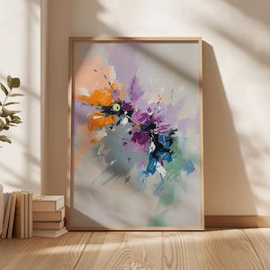May include: Abstract art print in a wooden frame. The artwork features a vibrant composition of brushstrokes in orange, purple, blue, and green against a gray background. The painting is displayed on a wooden floor, with a plant and books visible.