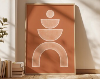 May include: Framed abstract art print featuring a terracotta background with a white geometric design. The design includes a circle, semi-circles, and an arch. The artwork is displayed on a wooden floor, leaning against a white wall.
