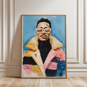Op de afbeelding: Waterverfportret van een persoon met een zonnebril, een zwarte coltrui en een kleurrijke jas. Het kunstwerk is ingelijst in een houten lijst en geplaatst tegen een lichtblauwe achtergrond.