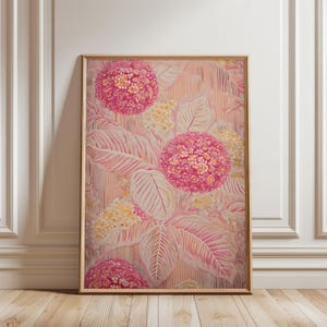 Op de afbeelding: Ingelijste bloemenkunstprint met grote roze en gele bloemclusters en oversized bladeren. Het kunstwerk heeft een zacht, getextureerd uiterlijk met een lichtroze en crèmekleurig kleurenpalet. De lijst heeft een lichte houttint.