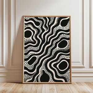 Op de afbeelding: Ingelijste abstracte kunstprint met een zwart-wit ontwerp. Het kunstwerk toont organische vormen, waaronder golvende lijnen, stippen en ovale vormen op een crèmekleurige achtergrond. De houten lijst complementeert het neutrale kleurenpalet.