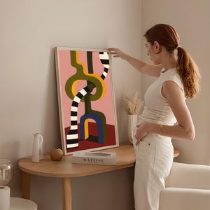 Contemporary abstract artwork featuring bold interlocking geometric shapes in olive green, gold, navy, and black-and-white stripes on a pink and red background.