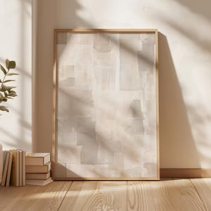 Può includere: Una stampa artistica astratta incorniciata con una tavolozza di colori neutri beige, crema e grigio. L'opera d'arte ha un aspetto strutturato con forme rettangolari sovrapposte. La cornice in legno completa l'opera, appoggiata a un muro con luce naturale.