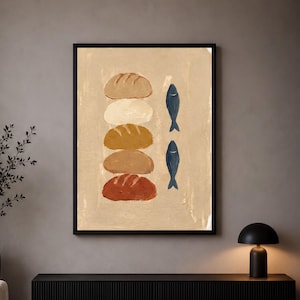May include: A framed wall art print featuring a vertical stack of five rounded loaves of bread in varying shades of tan, brown, and rust, positioned next to two dark blue fish illustrations, all set against a textured light beige background.