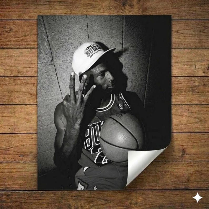 A black and white photograph of a basketball player wearing a Chicago Bulls jersey and cap, holding a basketball and making a peace sign gesture.