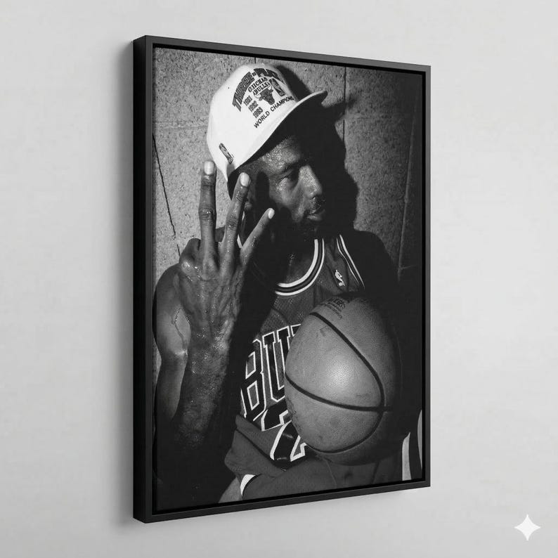 A black and white photograph of a basketball player wearing a Chicago Bulls jersey and a white cap, holding a basketball and making a peace sign gesture.