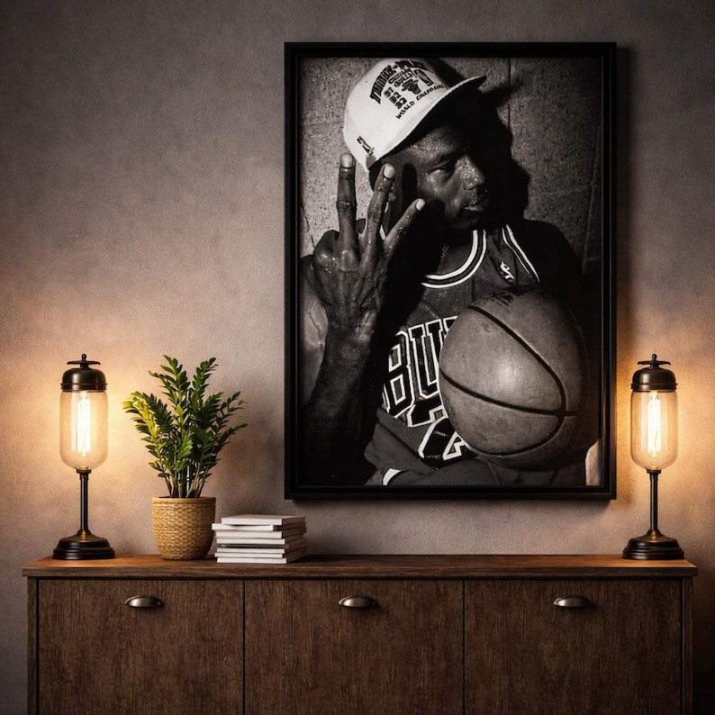 a framed black and white photograph of a man holding a basketball, with a potted plant and a stack of books on a wooden dresser below the frame.