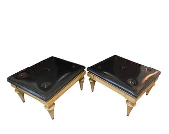 May include: A pair of low stools featuring rectangular, glossy black tufted tops and light-colored wooden frames. Each stool is supported by four tapered, cone-shaped legs that extend outward from the base, providing a stable foundation.