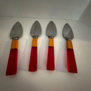 May include: Four cheese knives with stainless steel blades and vibrant handles. The handles transition from a yellow-orange section to a translucent red, creating a striking visual contrast. These knives are designed for serving cheese.