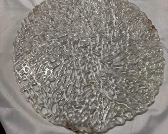 May include: A clear glass serving tray with a textured, raised design resembling coral. The tray is round and has a slightly irregular edge.
