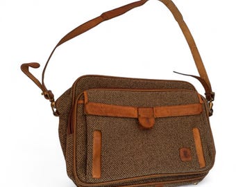 May include: A brown tweed shoulder bag with leather accents. The bag features a long, adjustable leather strap and a flap closure with a buckle. The bag has a rectangular shape and a small logo on the front.