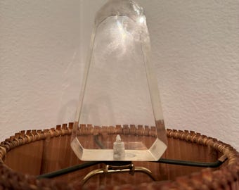 May include: A close-up of a lamp with a clear, geometric finial. The lampshade is a warm brown color with a woven texture. The lamp has a brass-colored metal frame.