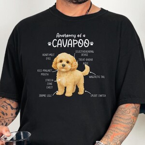 May include: Black t-shirt with a graphic of a Cavapoo dog and its anatomy labelled. The labels include "Heart-Melt Eyes," "Kiss-Magnet Mouth," and "Wagtastic Tail." The text "Anatomy of a Cavapoo" is above the dog illustration.