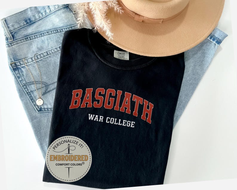 Puede incluir: Camiseta negra con el texto "BASGIATH WAR COLLEGE" en letras rojas. La camiseta se combina con vaqueros azul claro y un sombrero color canela. Una pegatina redonda con el texto "PERSONALIZE IT! EMBROIDERED COMFORT COLORS" est&aacute; en la camiseta.