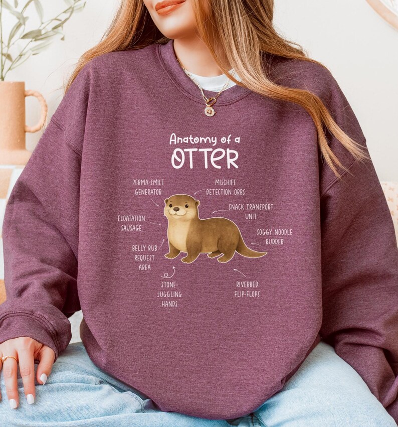 Puede incluir: Una sudadera granate con el texto "Anatomy of an Otter" y una ilustraci&oacute;n de una nutria con partes del cuerpo etiquetadas. La sudadera es de color liso y tiene mangas largas.