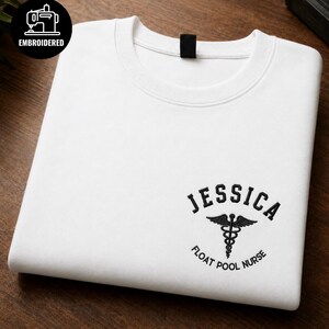 Könnte beinhalten: Ein weißes Sweatshirt mit Rundhalsausschnitt und schwarzer Stickerei auf der Brust. Das Design zeigt den Namen JESSICA in einem Bogen über einem Caduceus-Symbol, wobei der Text FLOAT POOL NURSE in einer serifenlosen Schrift darunter steht.