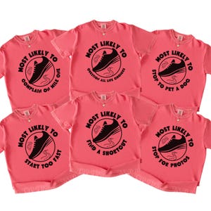 May include: Six coral-colored t-shirts with black graphic designs. Each shirt features a circular design with the text "Most Likely To" and a phrase such as "Complain on Mile One" or "Stop to Pet a Dog".