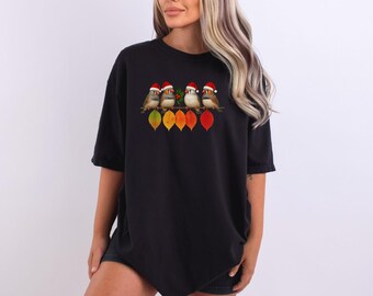 May include: Black t-shirt featuring a colorful graphic of four birds wearing Santa hats perched on a branch with autumn leaves. The birds are brown, white, and gray. The leaves are yellow, orange, and red.