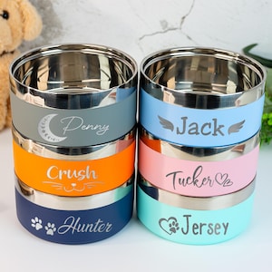 Puede incluir: Una pila de seis cuencos para mascotas de acero inoxidable con bandas de colores gris, naranja y azul. Cada cuenco est&aacute; grabado con el nombre de una mascota y un icono decorativo. Los cuencos son para comida o agua.