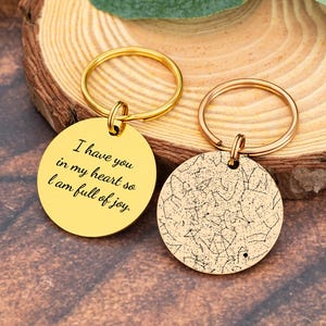 May include: Two gold-coloured keychains. One keychain has the text "I have you in my heart so I am full of joy." The other keychain has a constellation design. Both keychains have a gold ring.