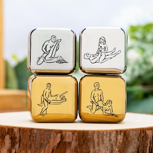 Può includere: Quattro dadi metallici con angoli arrotondati, impilati in due file. I due dadi superiori sono argentati e i due inferiori sono dorati. Ogni dado presenta un disegno a tratto nero raffigurante diverse posizioni sessuali. I dadi sono esposti su una superficie di legno.