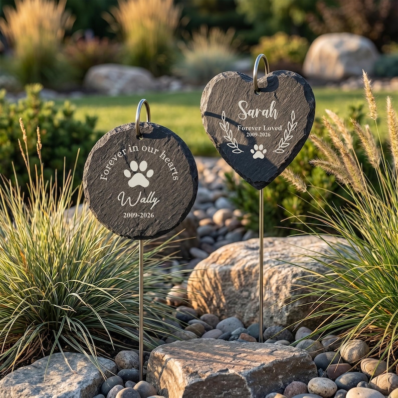 May include: Two memorial garden stones, one round and one heart-shaped, with engraved text and paw prints. The round stone reads "Forever in our hearts" and "Wally 2009-2026." The heart-shaped stone says "Sarah Forever Loved 2009-2026."