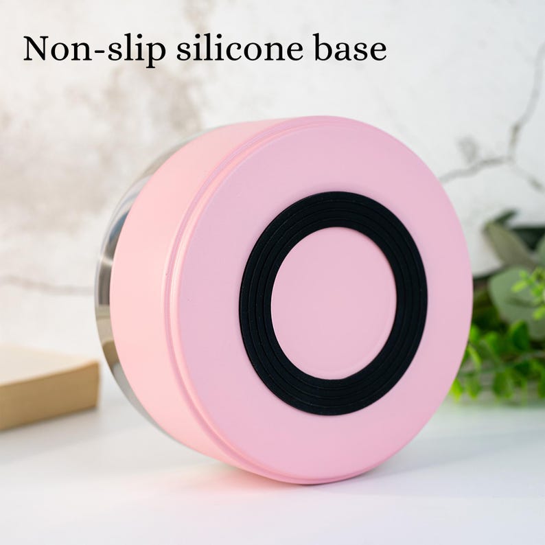 Puede incluir: Un recipiente rosa con una base de silicona antideslizante negra. El texto "Non-slip silicone base" es visible en la parte superior. El recipiente tiene un cuerpo transparente y redondeado.