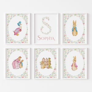 May include: Six framed art prints featuring watercolor illustrations of Peter Rabbit characters and floral designs. The prints include images of a duck, a rabbit, a fence, and a floral letter "S" with the name "Sophia". The frames are white.