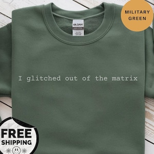 Puede incluir: Sudadera verde militar con el texto blanco "I glitched out of the matrix". Una pegatina redonda en la esquina superior derecha dice "Military Green".