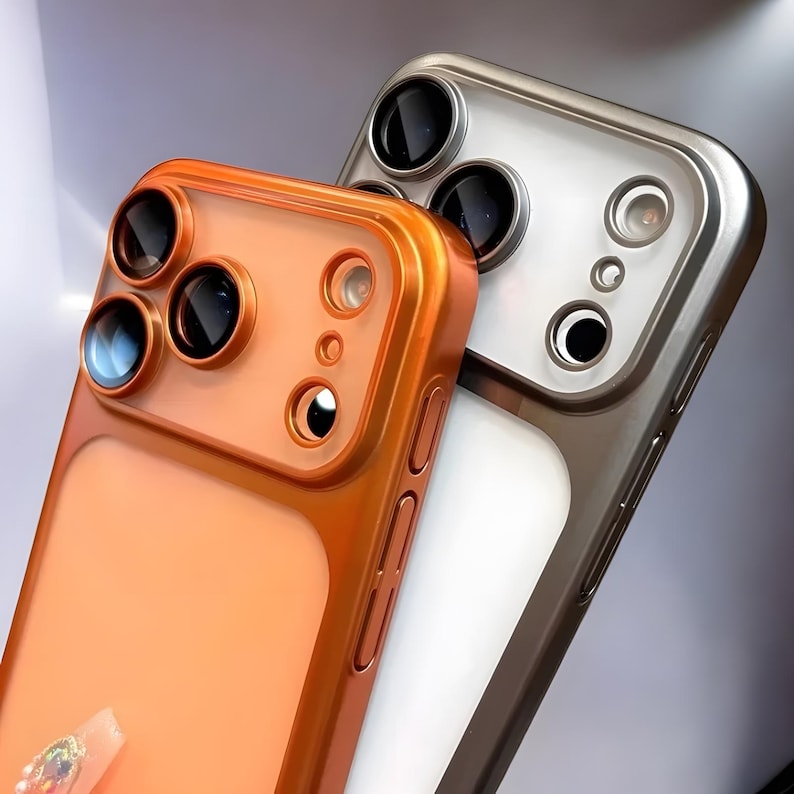May include: Two phone cases. One is a metallic orange color, and the other is silver. Both cases have a camera lens protector with multiple circular openings for the lenses. The orange case has a clear back.