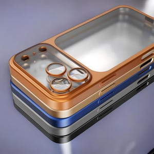 May include: A stack of phone cases in various colors: bronze, gold, blue, gray, and black. Each case has a clear, transparent section for the phone screen and circular cutouts for the camera lenses. The cases are stacked on a gradient purple background.