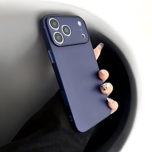 Puede incluir: Funda de teléfono azul marino con un módulo de cámara con tres lentes y un flash. La funda está sujeta por una mano con uñas cuidadas, mostrando un diseño elegante y moderno.