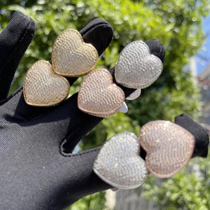 May include: Three pairs of heart-shaped earrings with a sparkly, textured finish. The earrings are in gold, silver, and rose gold.