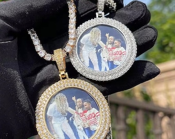 May include: Two diamond-encrusted pendant necklaces. One has a gold setting, the other silver. Each pendant features a circular frame of small diamonds surrounding a photograph. The chains are also adorned with diamonds.