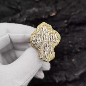 Puede incluir: Un anillo de oro con forma de cruz con un gran diseño de piedras rectangulares transparentes.