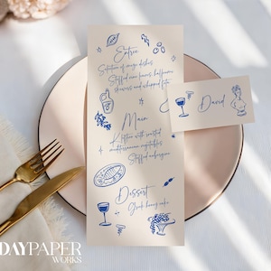 Op de afbeelding: Een menu en een naamkaartje met blauwe illustraties en tekst op een crèmekleurige achtergrond. Het menu bevat voorgerechten, hoofdgerechten en desserts. Een gouden vork en mes liggen op een wit servet. Het naamkaartje heeft de naam "David".