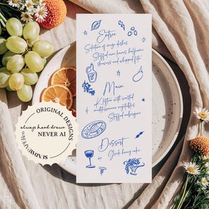 May include: A white menu card with blue handwritten text and illustrations, showcasing a Greek menu with dishes such as stuffed vine leaves and Greek honey cake. The card is on a white plate, surrounded by flowers and fruit.