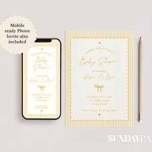Może przedstawiać: Zestaw zaproszeń na baby shower, w tym smartfon wyświetlający zaproszenie, pasującą kartę i oł&oacute;wek. Zaproszenie ma kremowe tło ze złotym tekstem i grafiką kokardy. Tekst brzmi "Baby Shower".