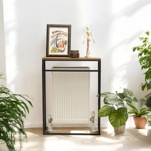 May include: A black metal radiator cover with a wooden top shelf. The shelf has a framed print, a wooden figurine, and a small jar. The radiator cover is in front of a white wall.