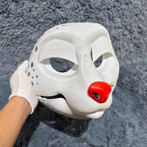 May include: White furry animal mask with a red nose and black eyes. The mask is made of a smooth, hard material and has a textured surface.