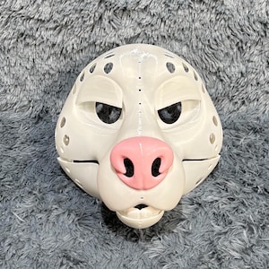 May include: White furry animal mask with pink nose and black eyes. The mask has a textured surface and is made of a hard material.