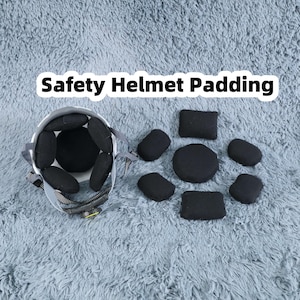 May include: A white safety helmet with black padding and straps, alongside several individual black padding pieces. The text "Safety Helmet Padding" is displayed in white letters.