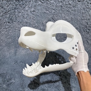 May include: White unpainted 3D printed animal mask with a large open mouth and sharp teeth. The mask has a hole for the eyes and is made of a smooth plastic.