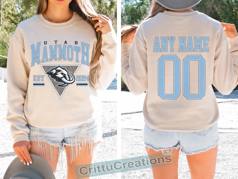 Puede incluir: Sudadera beige con "UTAH MAMMOTH" en letras azul claro y un logotipo de mamut. La parte trasera presenta "ANY NAME" y el n&uacute;mero "00" en azul claro. Una prenda c&oacute;moda para los aficionados al deporte.