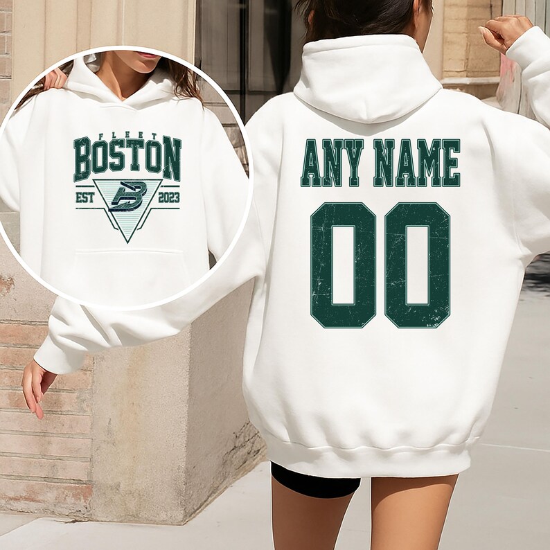 May include: White hoodie with a front pocket and drawstring. The front features the text "FLEET BOSTON" above a logo and "EST 2023". The back displays "ANY NAME" above the number "00" in a distressed green font.