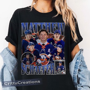 May include: Black t-shirt with a retro design, displaying the name "MATTHEW SCHAEFER" in blue. The shirt features multiple images of a hockey player in a blue and orange uniform, with the New York Islanders logo.
