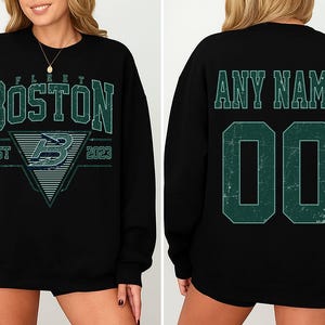 May include: Black sweatshirt with "BOSTON" in distressed green lettering. The front features a triangle design with a "B" and "EST 2023". The back has "ANY NAME" above the number "00" in green.