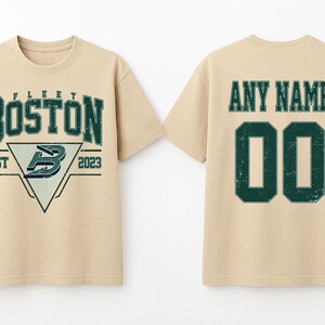 May include: A beige t-shirt with a distressed green graphic on the front that says "BOSTON" above a triangle with a "B" logo and "EST 2023". The back of the shirt has "ANY NAME" above the number "00".